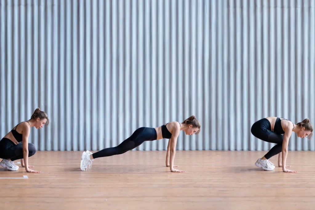 A woman performing burpees, transitioning from a squat to a plank position, as part of her exercises to lose belly fat at home.