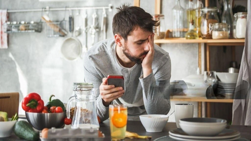 Man looking frustrated in the kitchen, surrounded by healthy food, reflecting on why he’s not losing weight in a calorie deficit despite efforts to maintain a balanced diet.