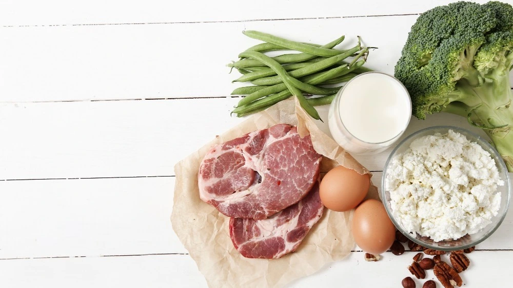 Meal prep ideas high protein – A flat lay of steak, eggs, milk, broccoli, green beans, cottage cheese, and nuts on a white wooden background for healthy meals.