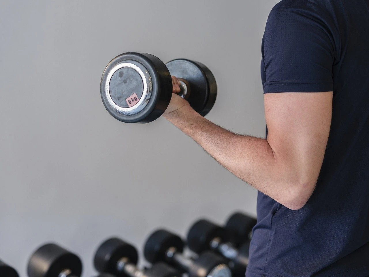 Man lifting a dumbbell in a gym setting, showcasing arm strength and fitness focus, ideal for learning about Bodyweight Bicep Exercises and building muscle at home.