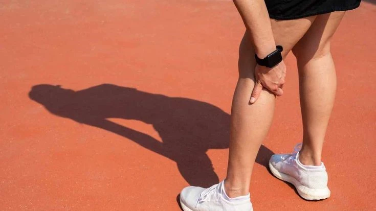 Person holding their hamstring muscle while stretching outdoors, demonstrating the importance of Bodyweight Hamstring Exercises for muscle health and injury prevention.