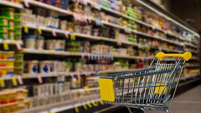 Shopping cart in a grocery store aisle with shelves stocked with food items, illustrating a well-planned High Protein Diet Grocery List for balanced meal preparation.