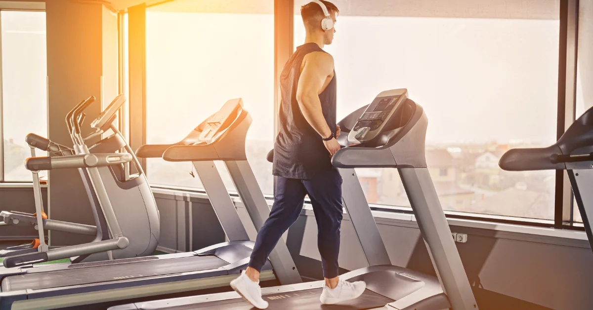 Man using a treadmill at the gym during sunrise, demonstrating a running machine exercise to lose weight with proper posture and focused intensity.