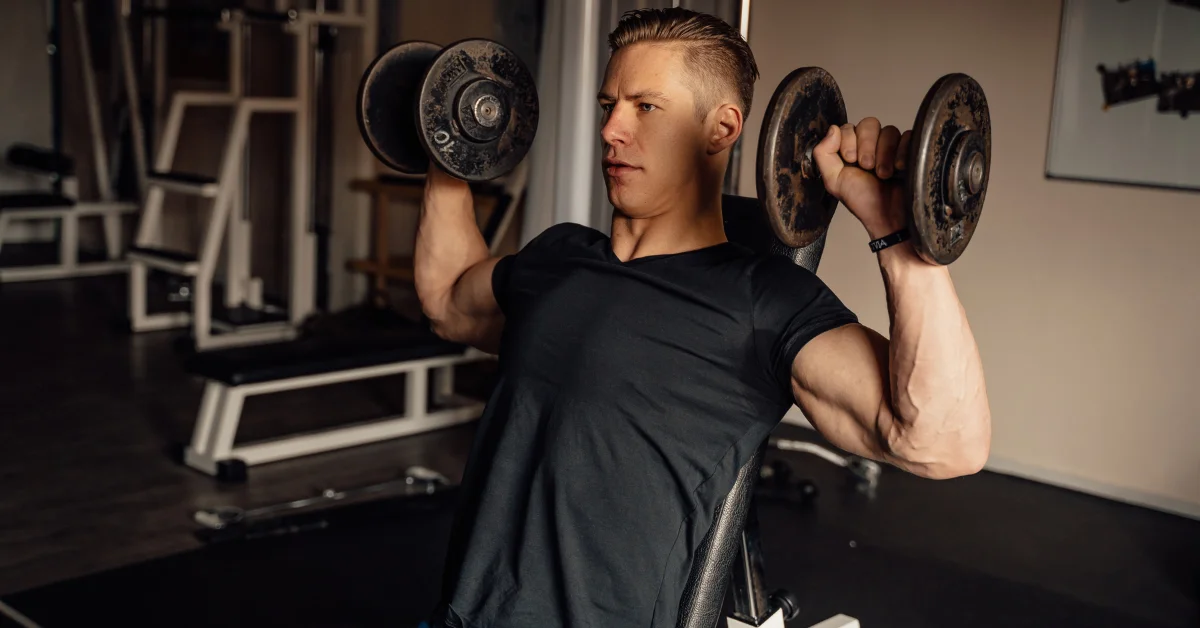 Man performing seated db military press with dumbbells in a gym to build shoulder strength and improve upper-body muscle balance.
