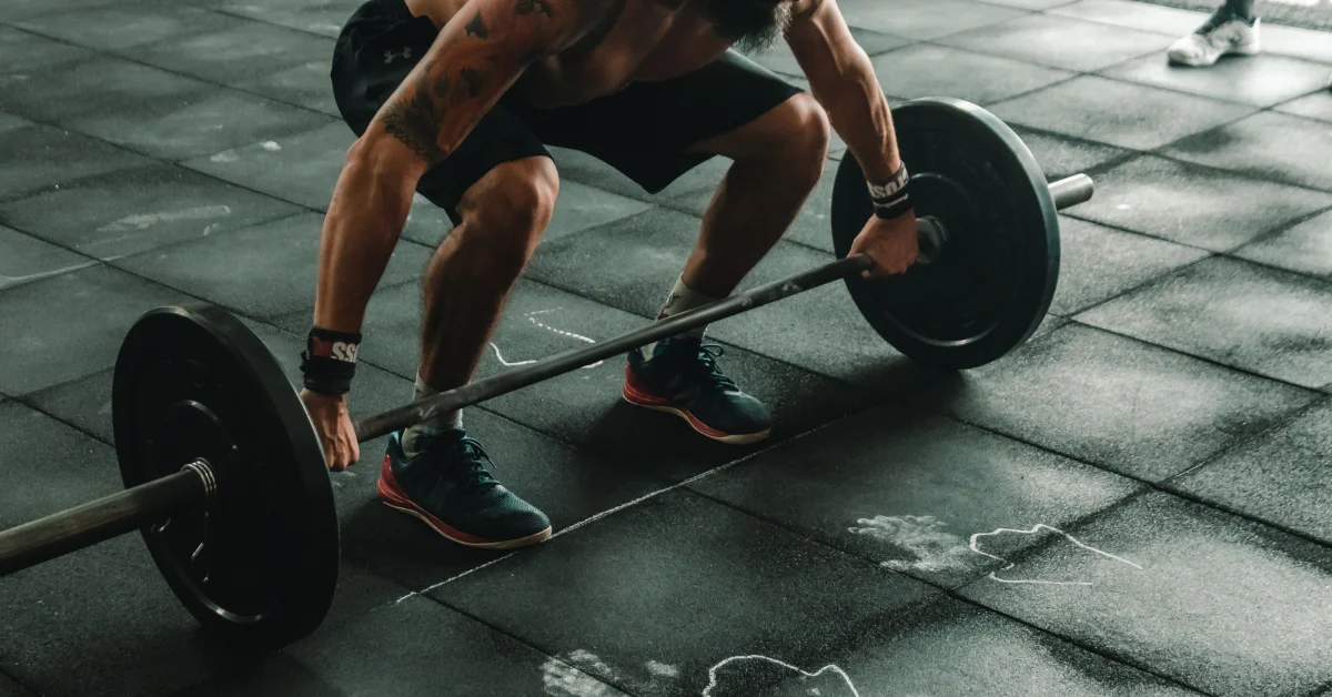 Man performing a barbell deadlift in a gym, showcasing proper lifting form with a loaded barbell on a rubber floor.